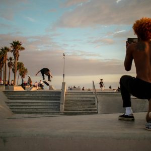 A skateboarder performs a trick at a vibrant skate park in Los Angeles during sunset.
