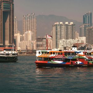 A vibrant ferry sails through Victoria Harbour with Hong Kong skyscrapers in the background.