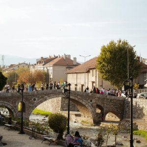 Scenic view of a historic stone bridge over a river in Prizren, Kosovo, with people walking and a charming urban backdrop.